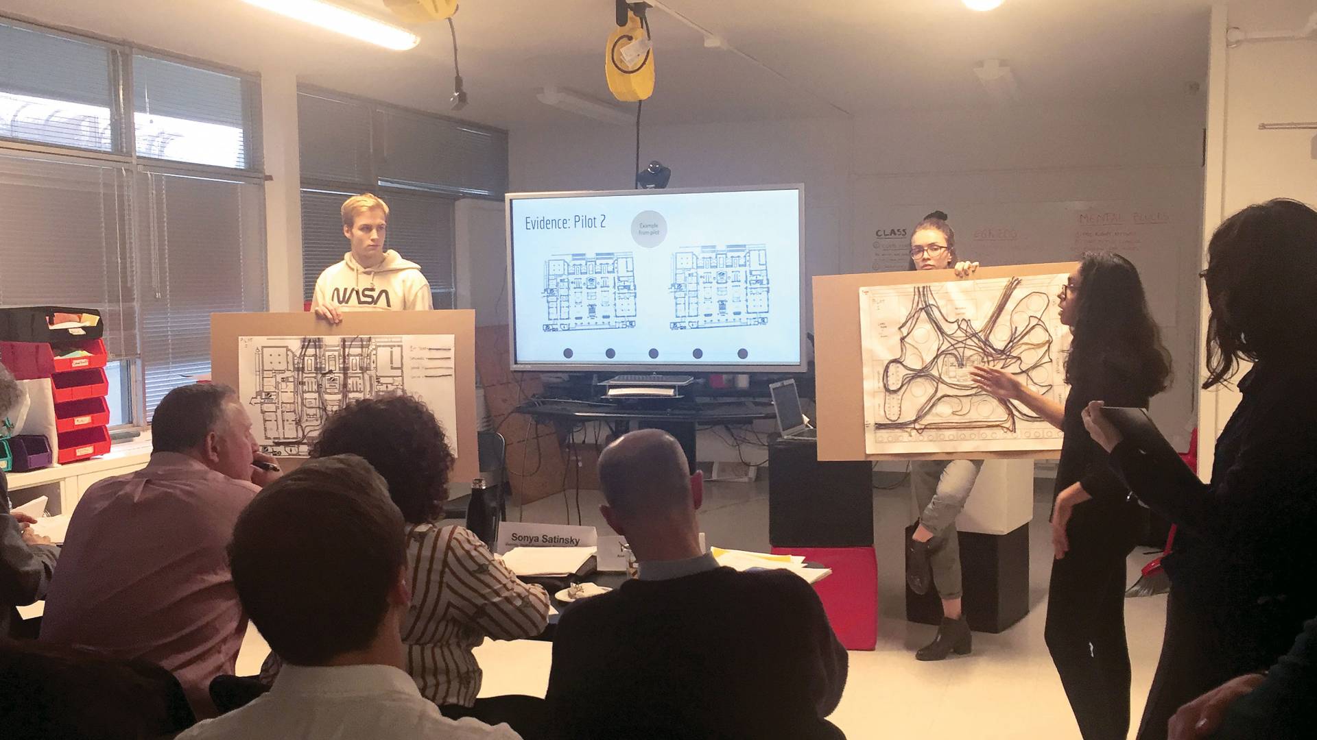 Two students presenting to a group in front of a video presentation