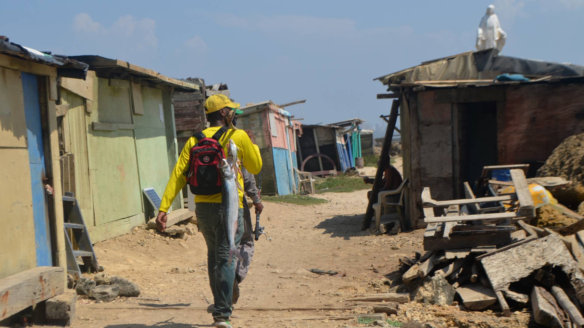 Man walking down dirt alley with string of fish on his back