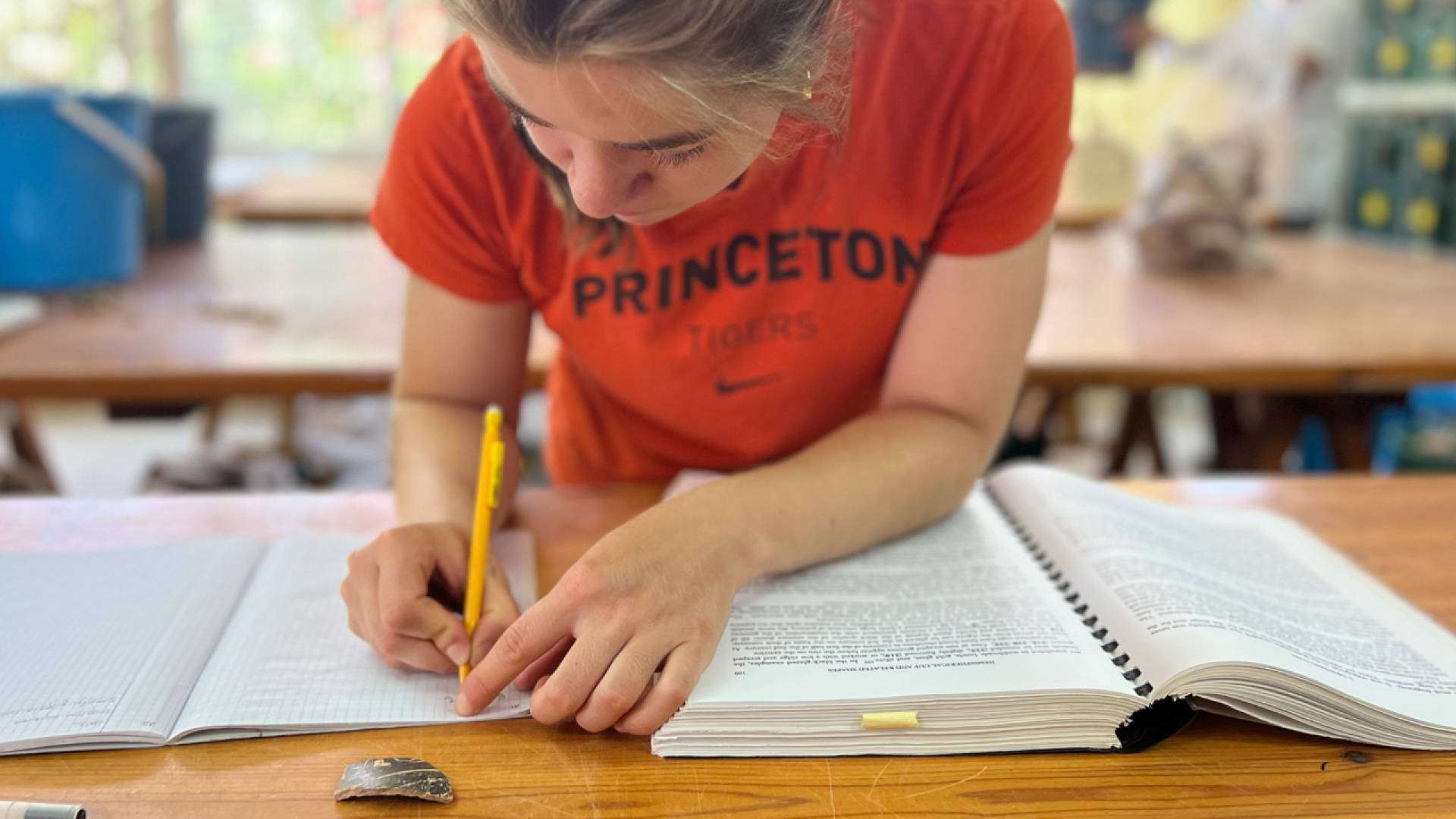 A student wearing an orange Princeton shirt is writing on her notebook,