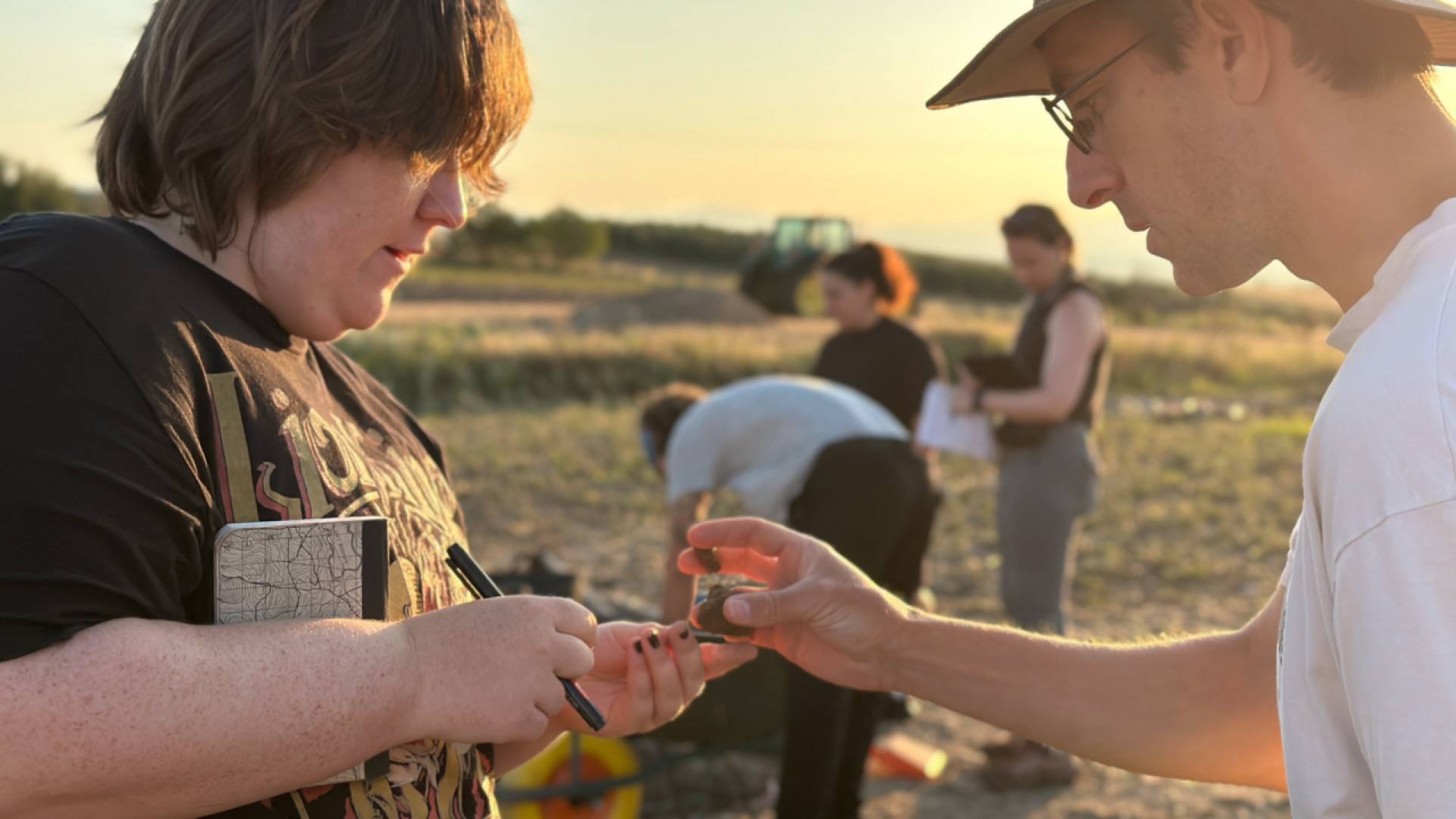 A student and Prof. Nathan examines a small piece of fragment in the middle of a field.