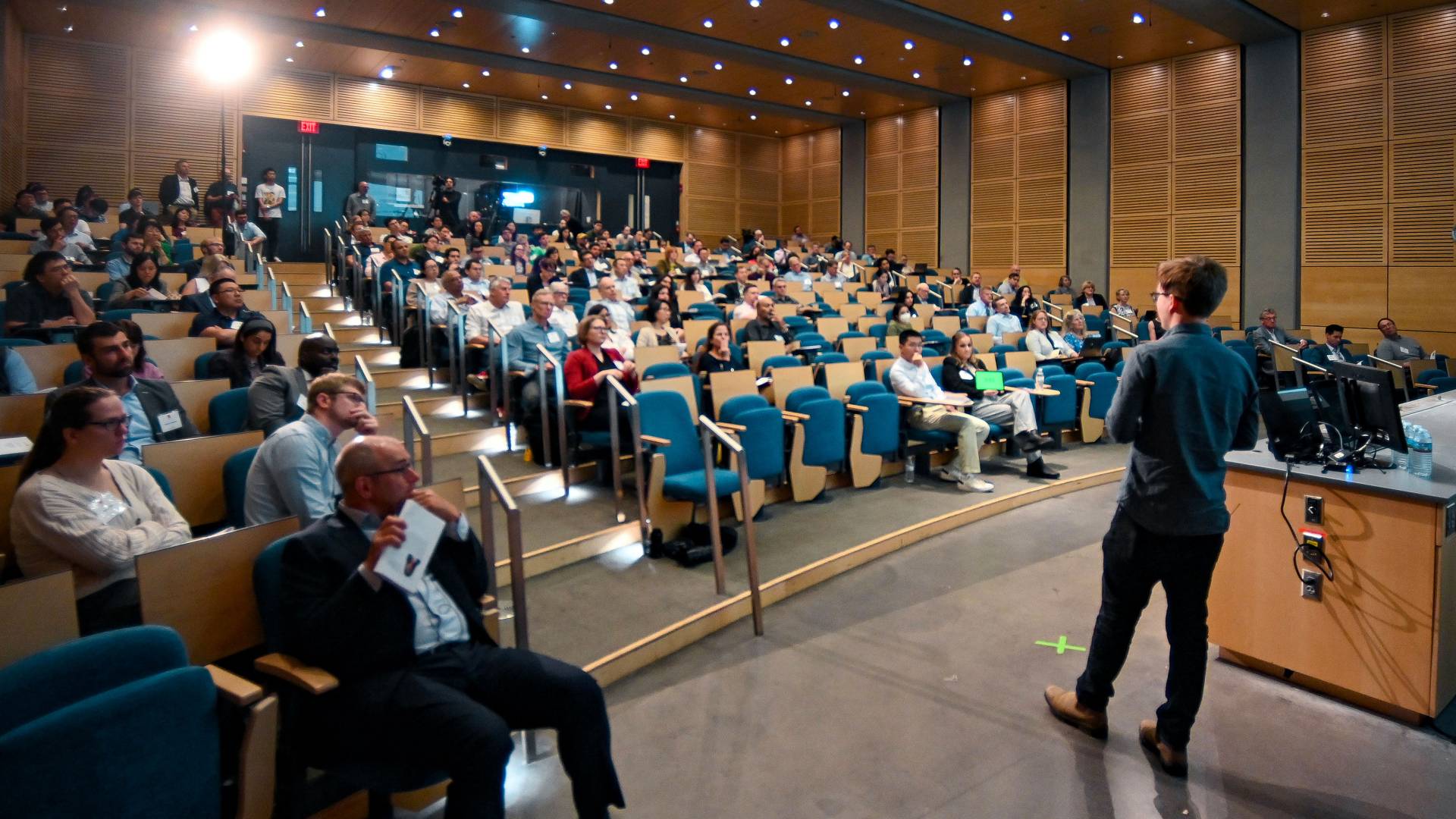 A speaker addressing a seated crowd in an auditorium