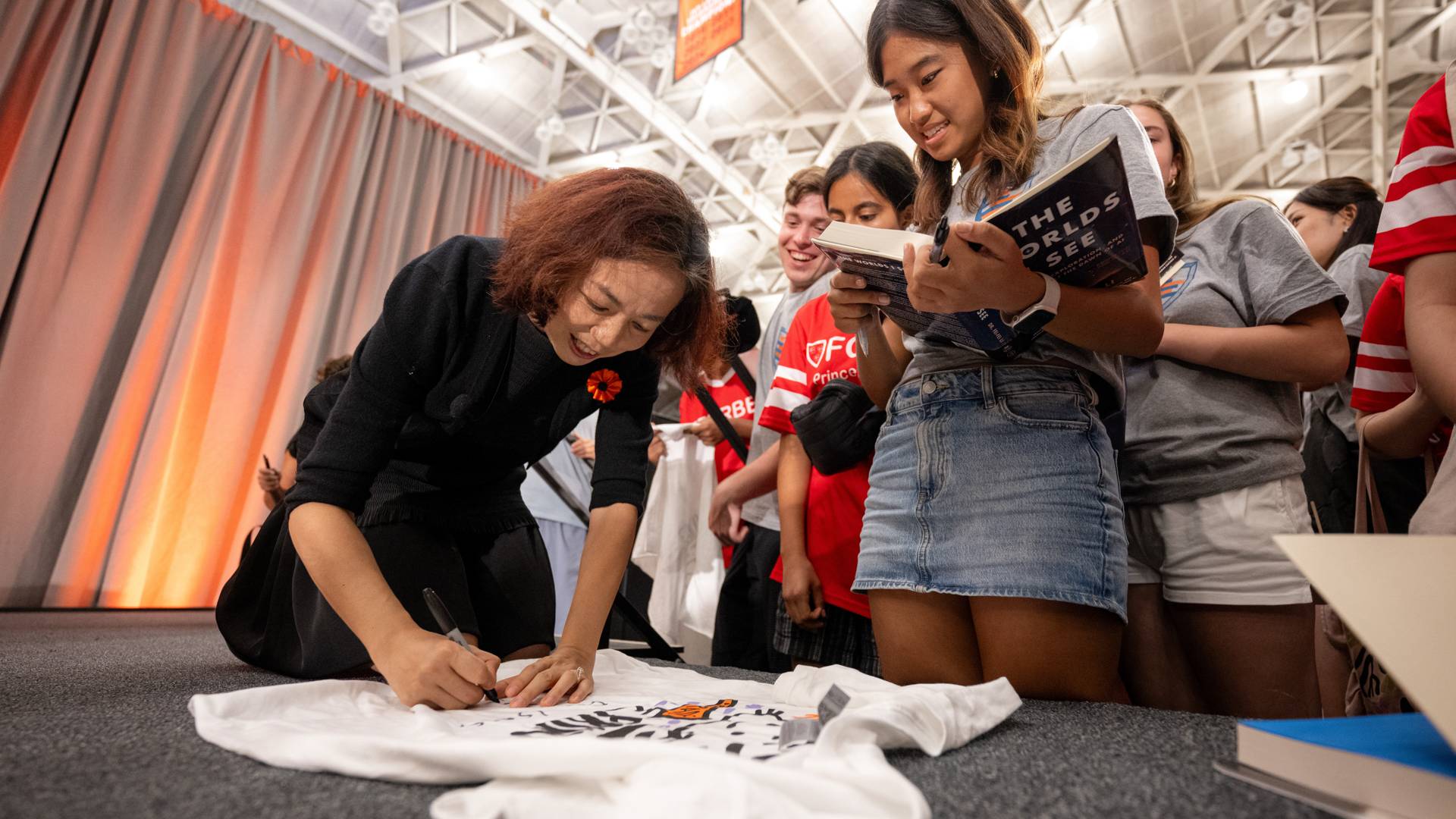 Fei-Fei Li signing a shirt surrounded by students
