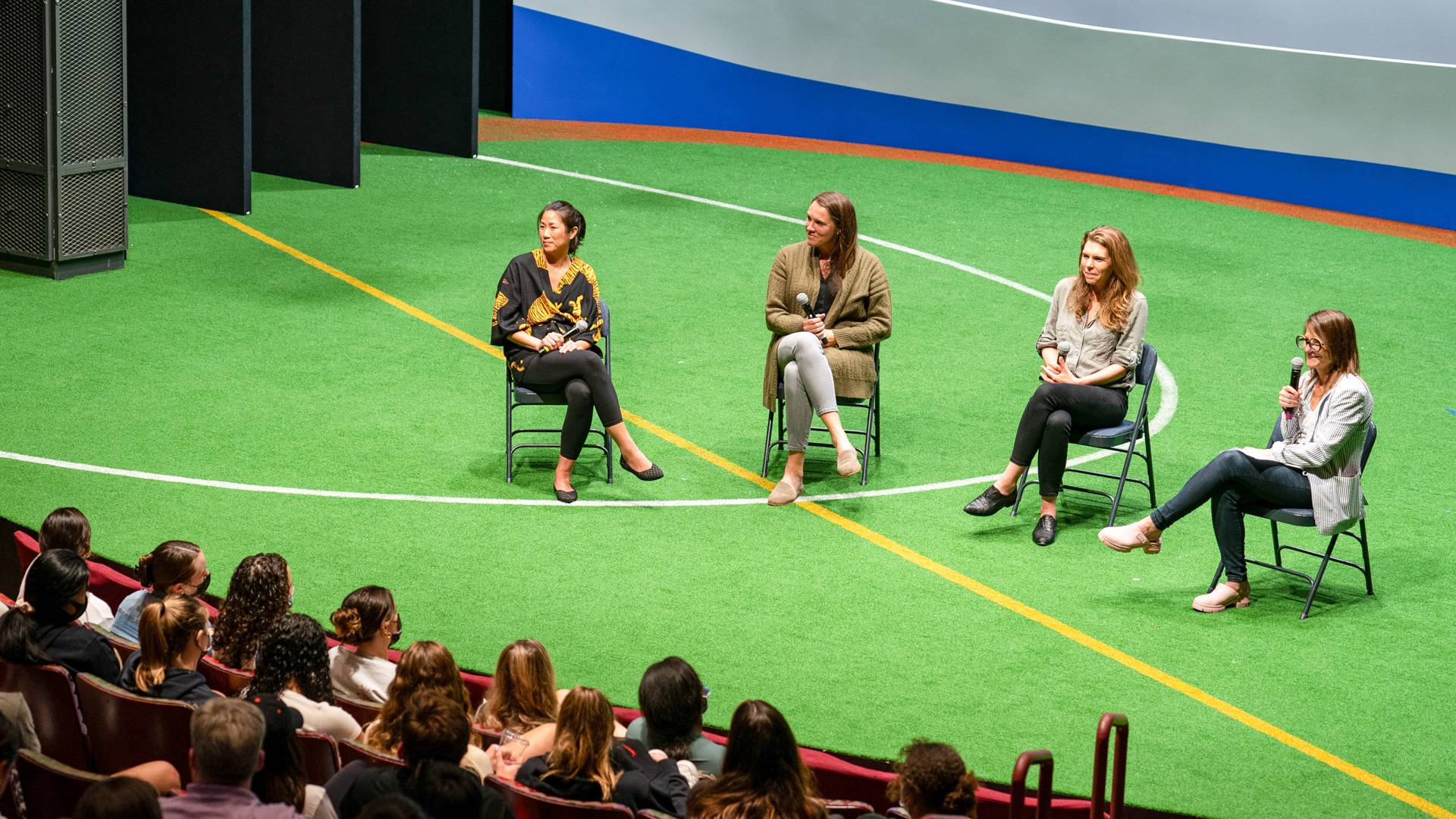 Four people sitting on a stage decorated as a football field.
