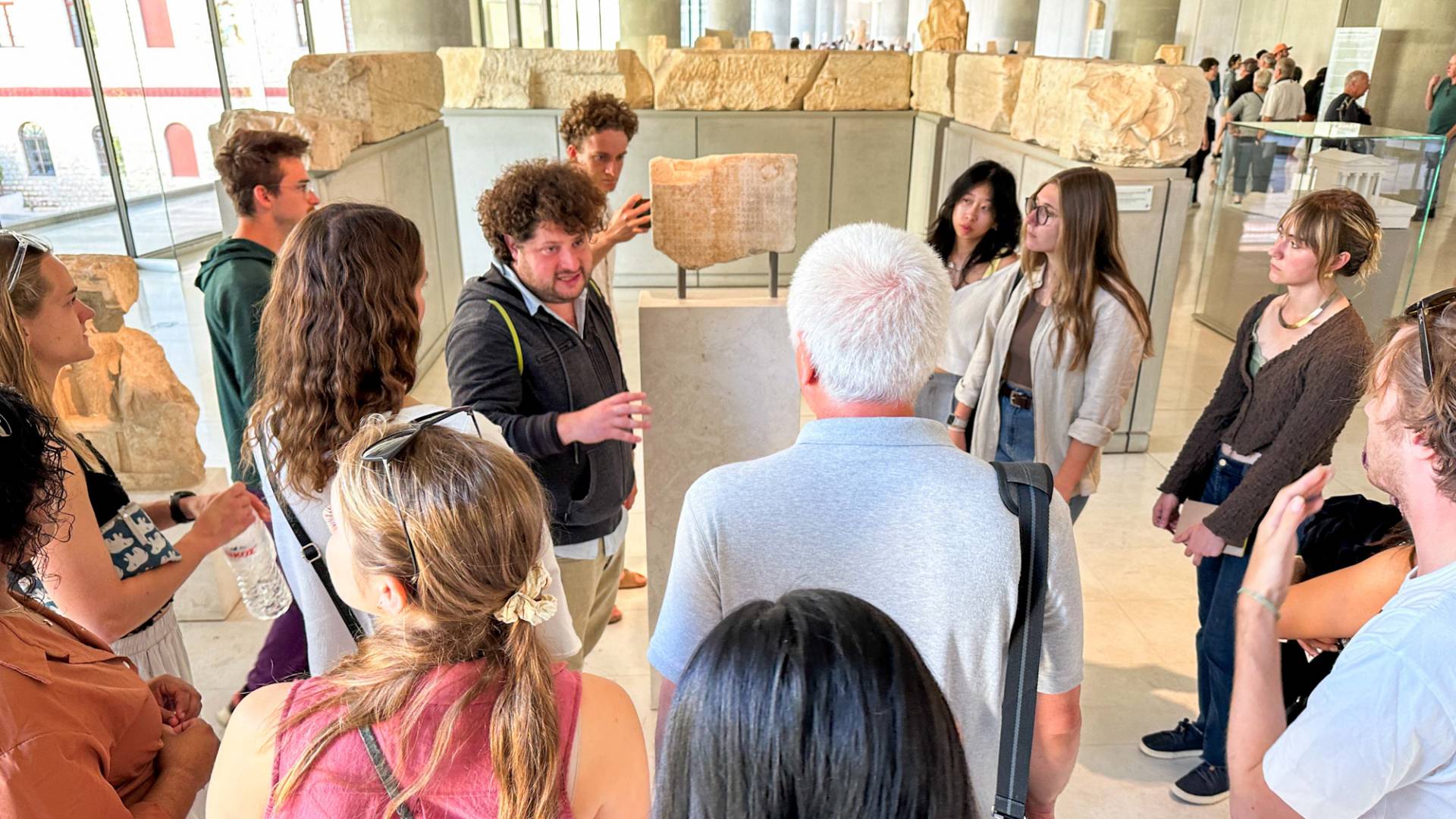 A man is talking to a group, surrounded by ancient ruins.