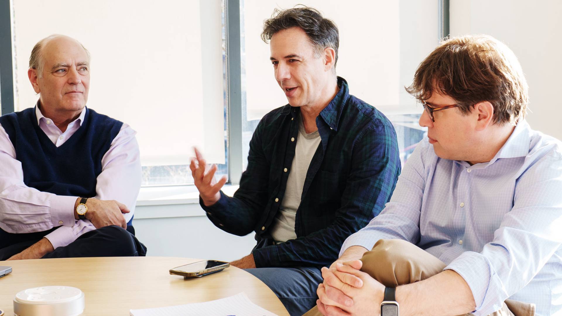 A man speaks at a table surrounded by colleagues.