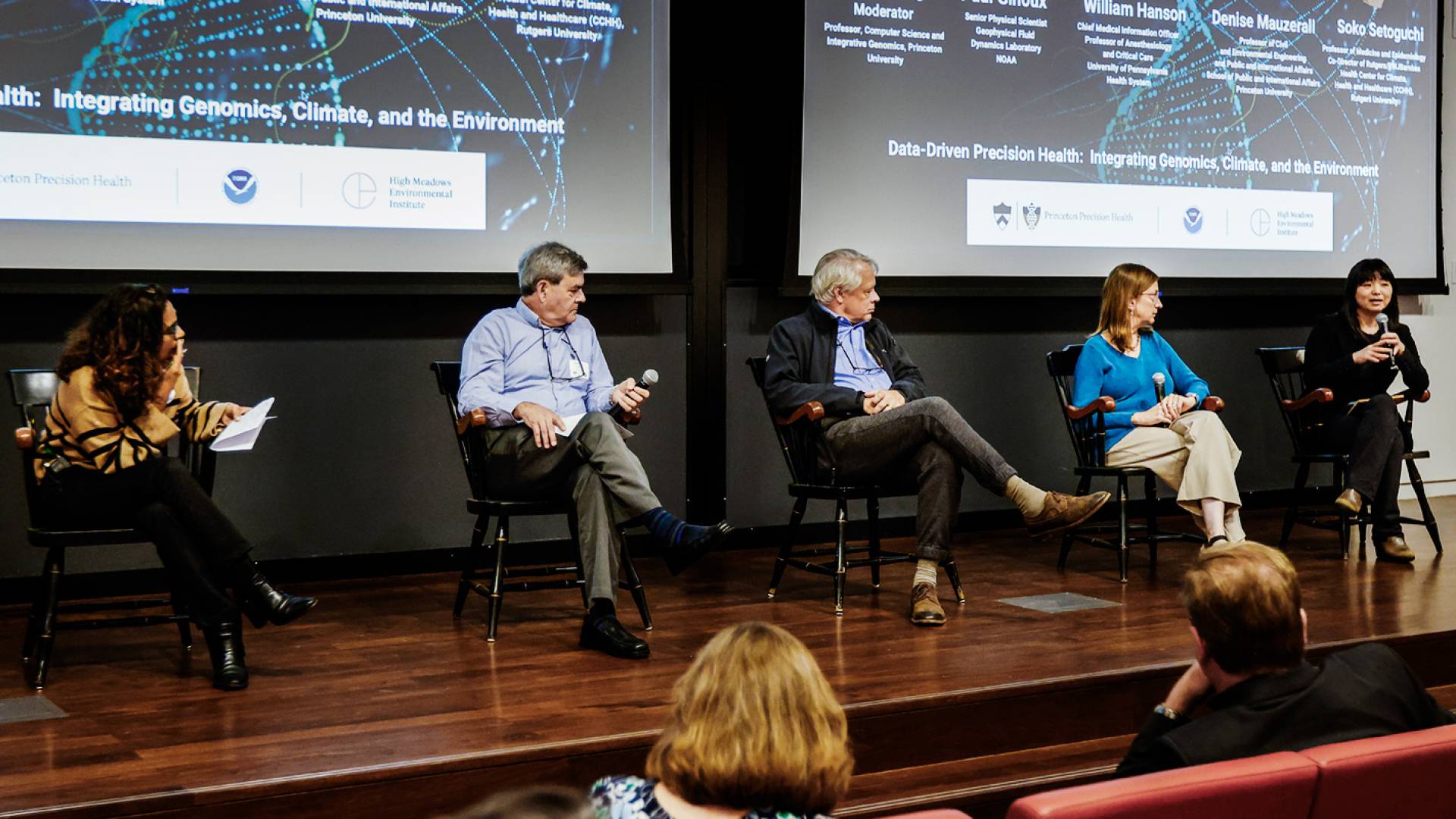 Moderator Mona Singh and three male panelists listen as a female panelist speaks into a microphone.