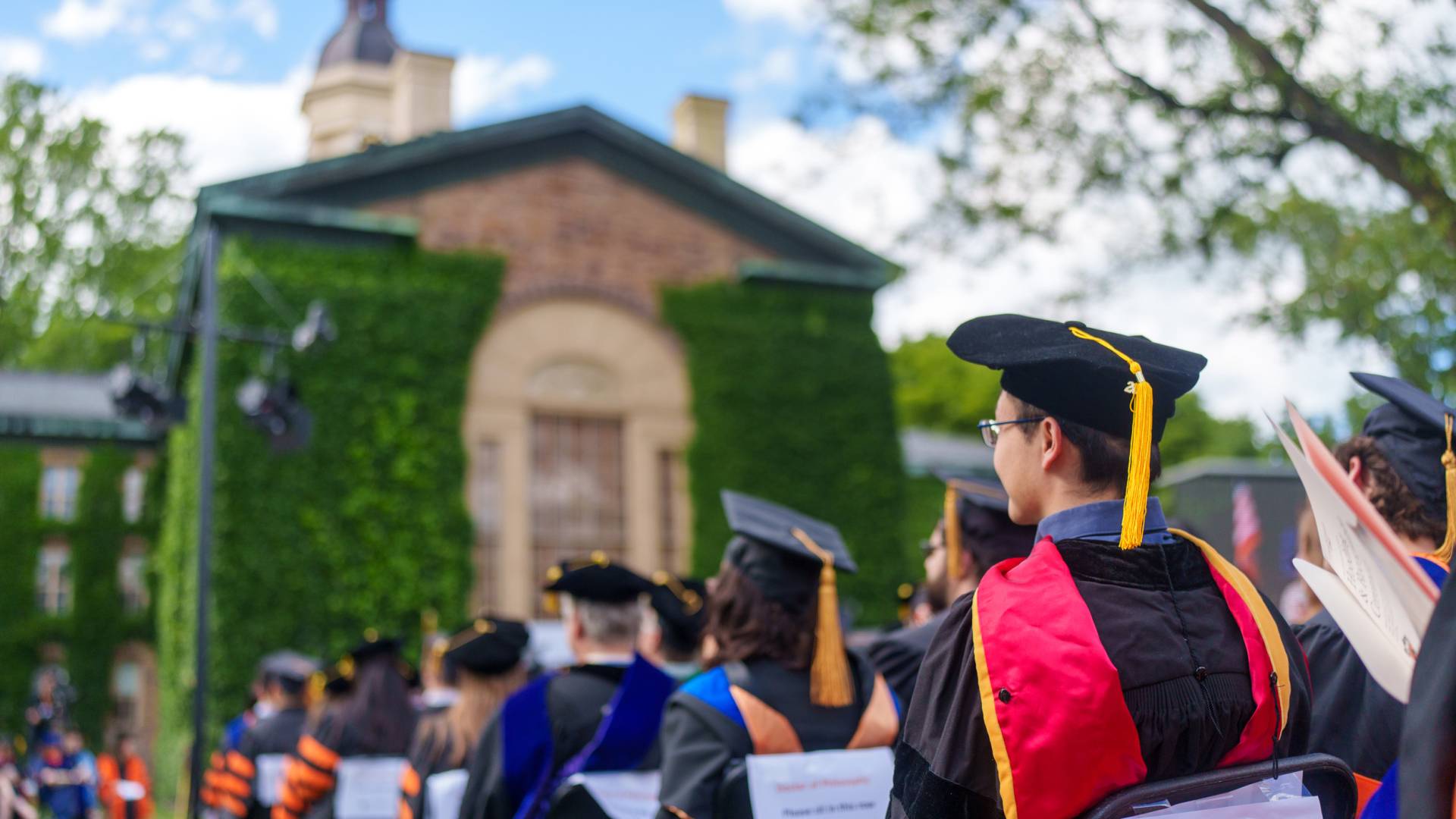 Students and professors in Ph.D. regalia look toward Nassau Hall from Cannon Green.