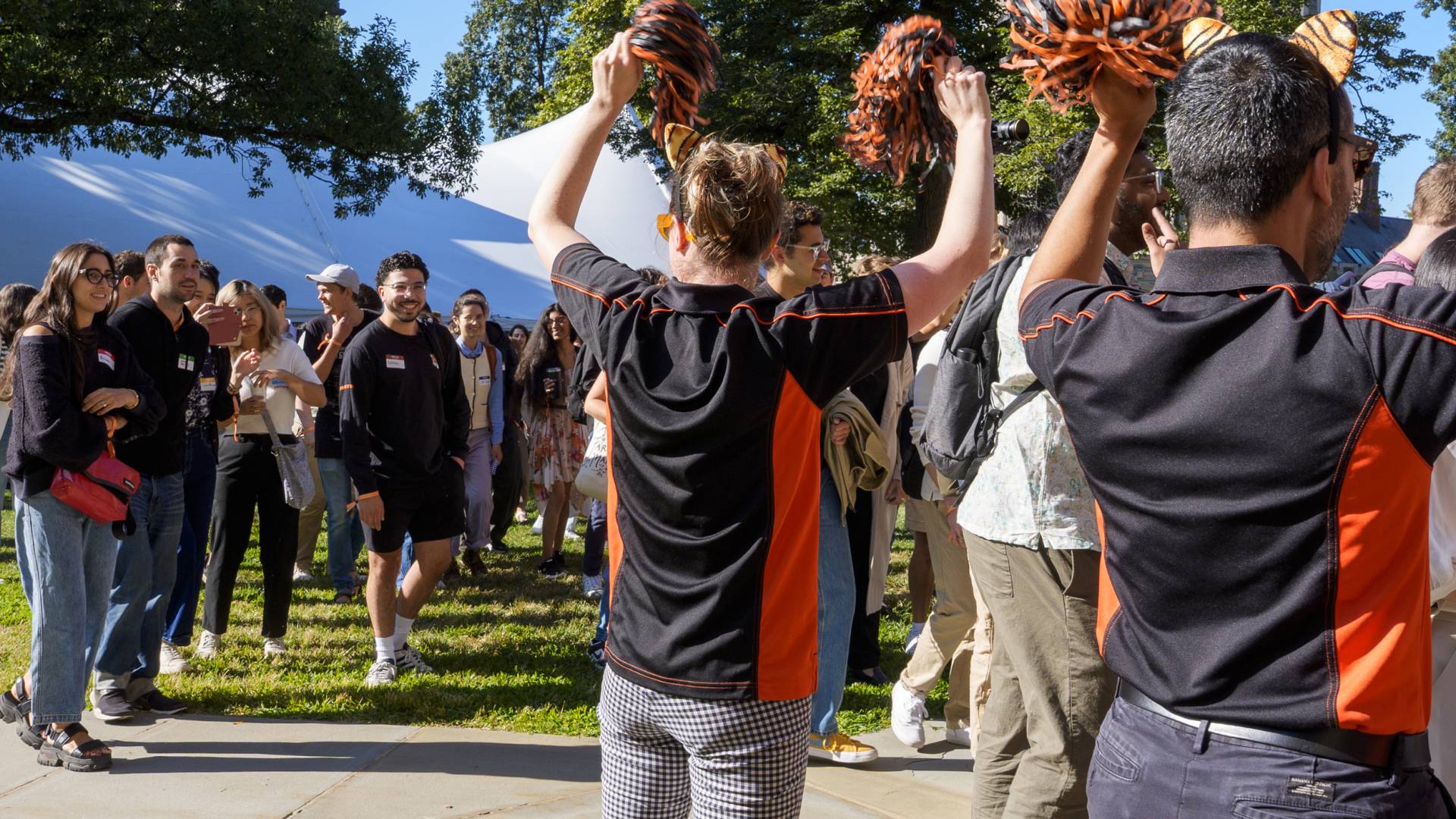 Graduate School staff wave orange and black pompoms and cheer as students arrive at Alexander Hall