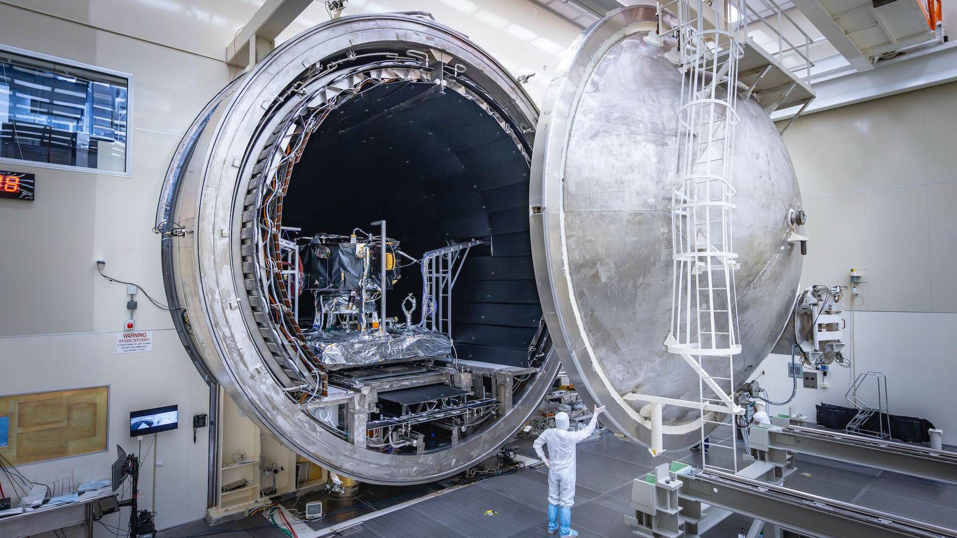 A small human figure indicates the scale of an enormous chamber holding the IMAP spacecraft.