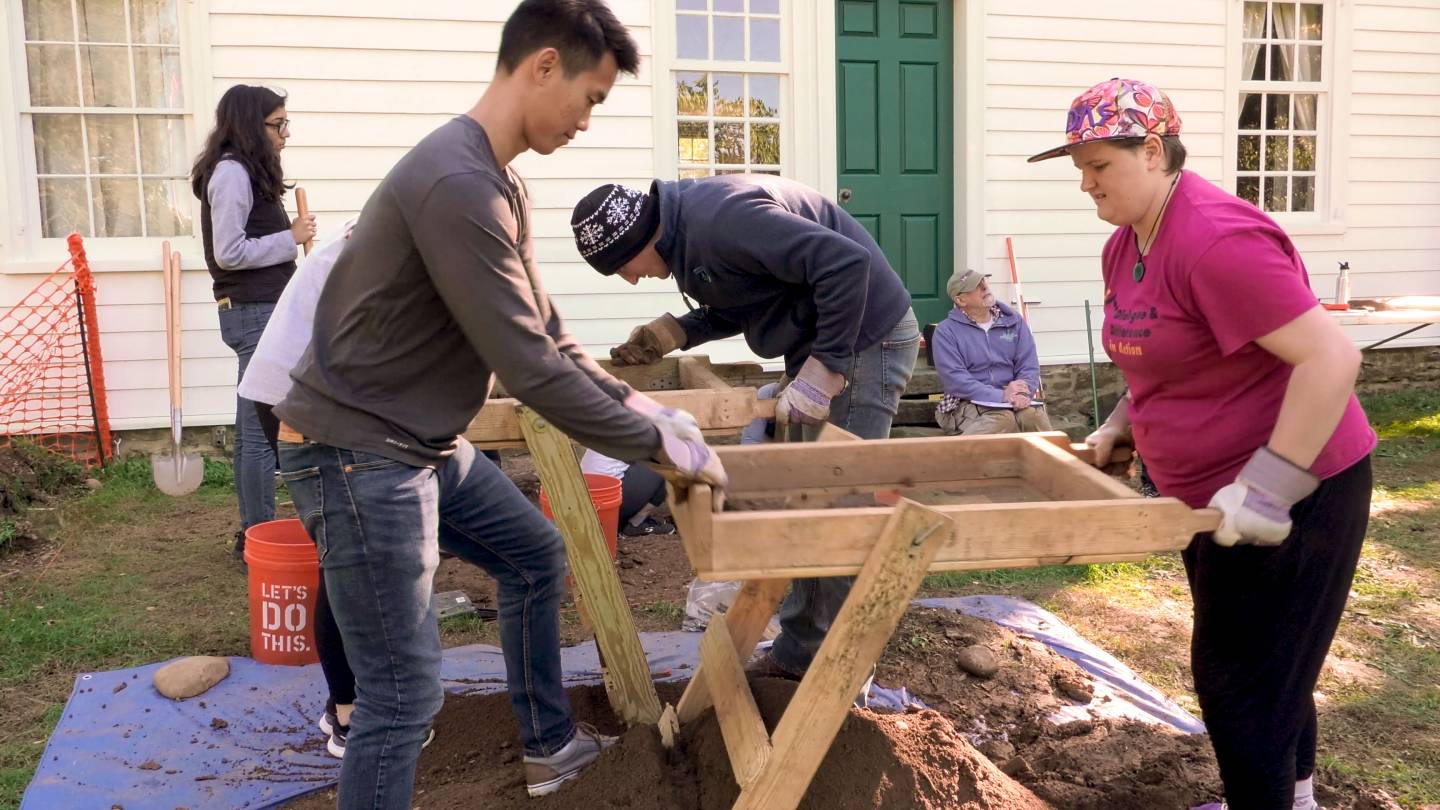 Students sifting soil through large wooden and wire mesh sifters