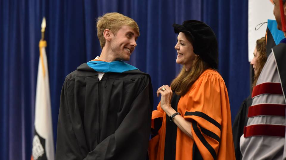 Student looks at Sandra Bermann as he receives his hood