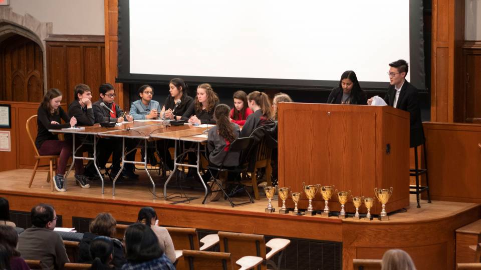 A team sits at a table on the stage, taking a question from moderators