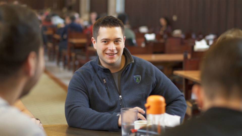 Tyler Eddy sitting a table in a dining Hall with friends