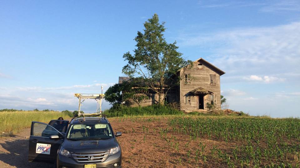 Mobile lab in front of farmhouse in a corn field