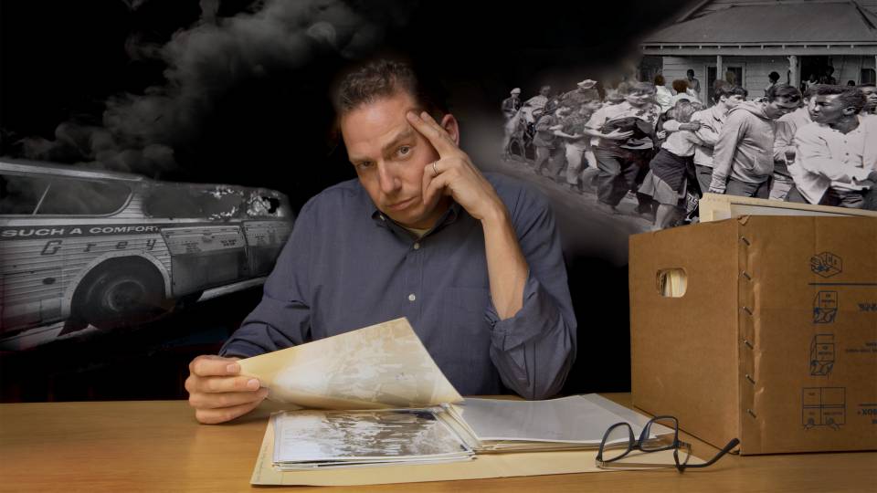 Kevin Kruse sitting at a table with archived material and scenes of the Civil Rights movement behind him