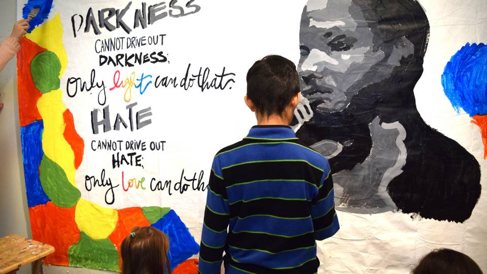 A child helps paint a mural with a quote from Martin Luther King: "Darkness cannot drive out darkness; only the light can do that. Hate cannot drive out hate; only love can do that."
