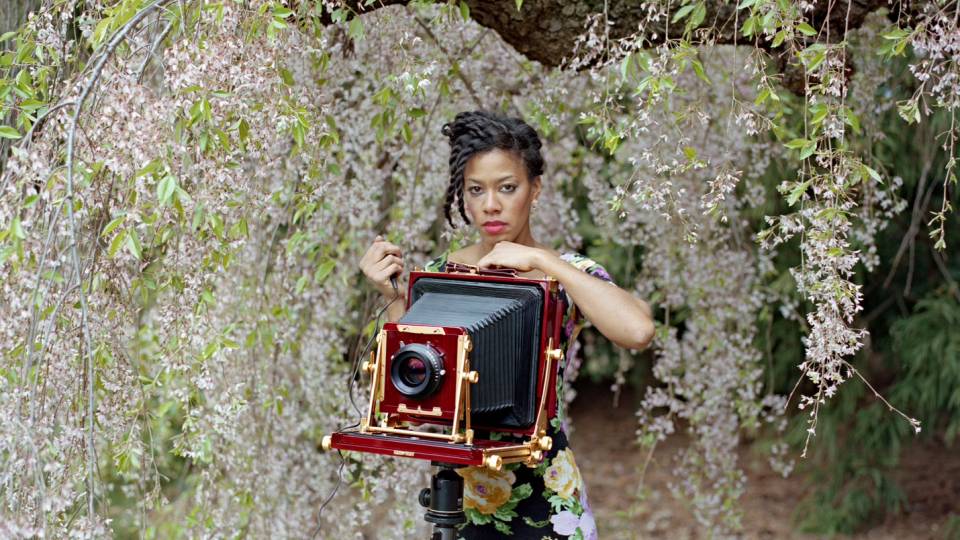 Deana Lawson behind a square-format camera amongst cherry blossoms