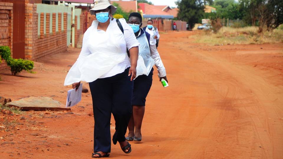 Women in masks walk along a road in Africa