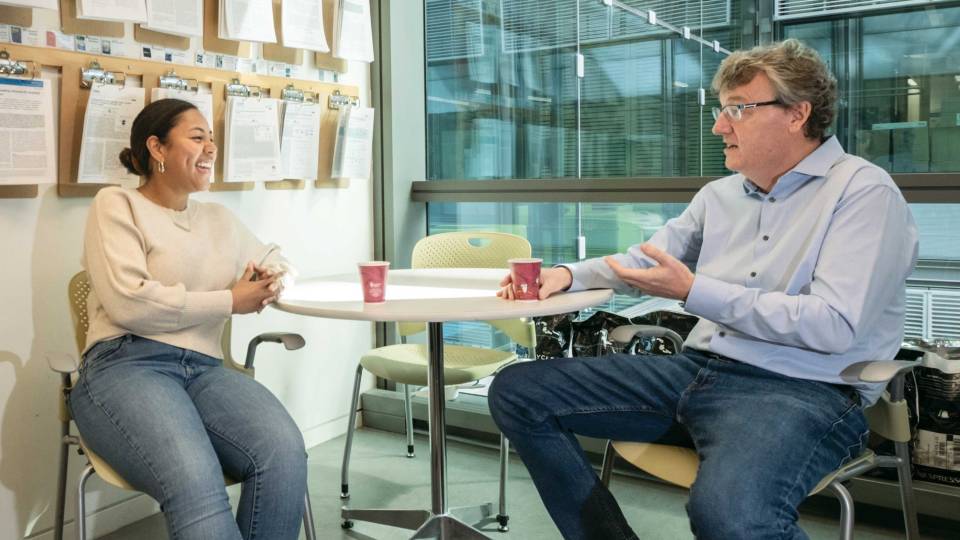 Cassidy Humphreys and David MacMillan having a conversation in front of a wall of papers