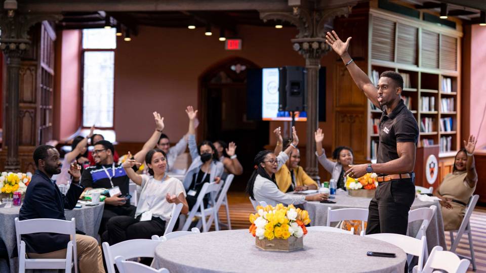 Isaac Serwanga raises his arm while speaking to an audience who are also raising their arms