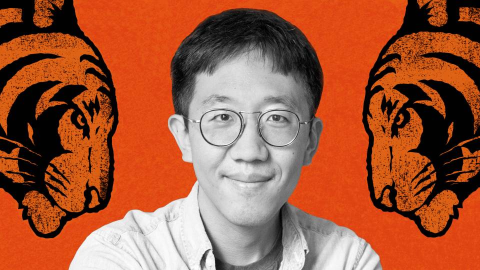 June Huh smiles in a light-colored shirt and round wire-framed glasses.