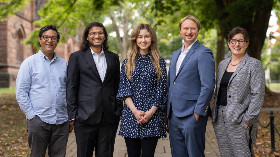 Five smiling computer scientists pose outside in professional attire.