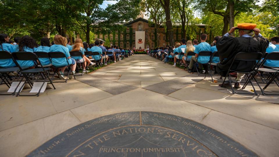 The backs of students seated in rows of chairs in front of Nassau Hall 