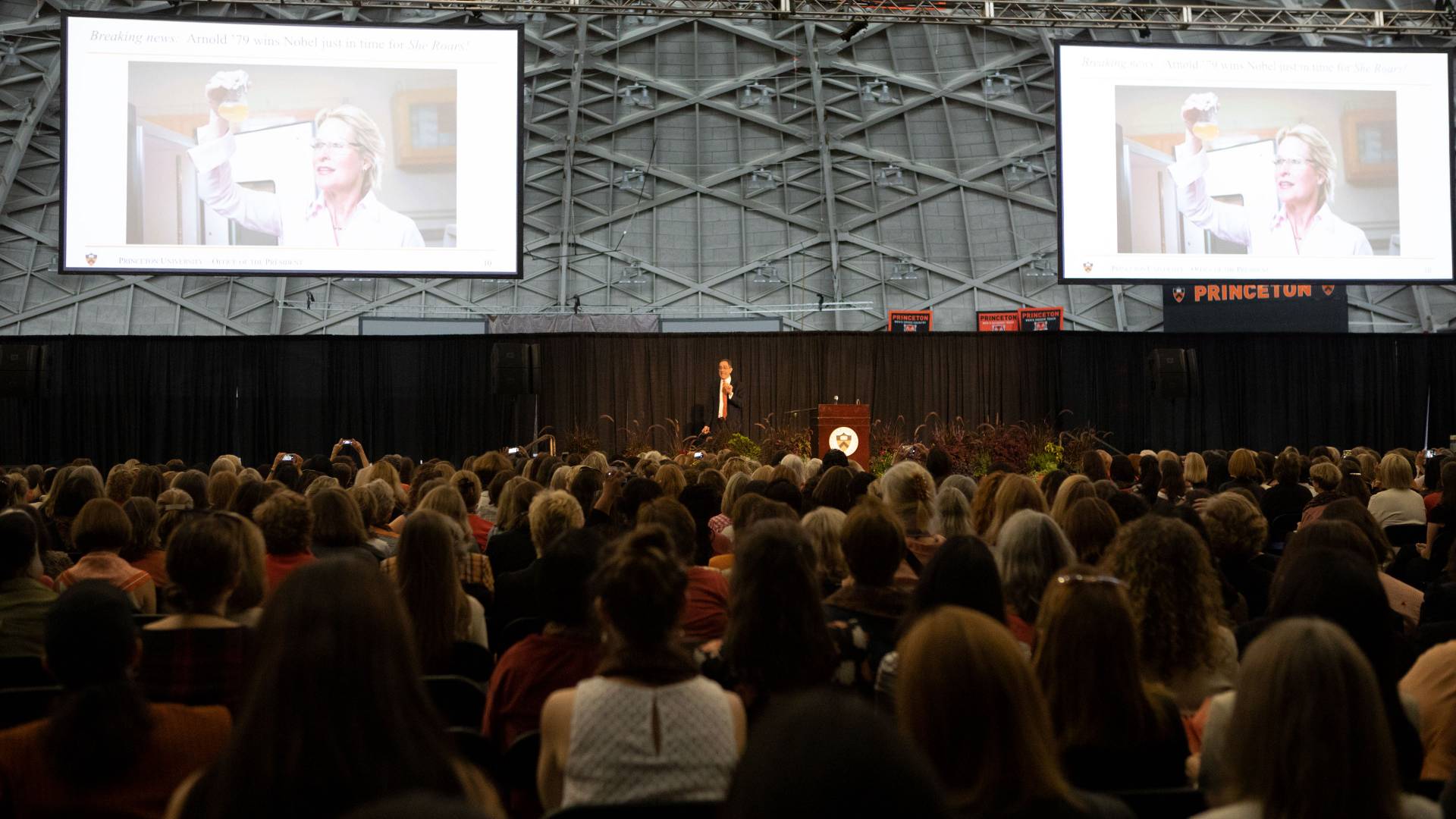 Overview of audience listening to President Eisgruber speak with photos of Frances Arnold projected on large screens