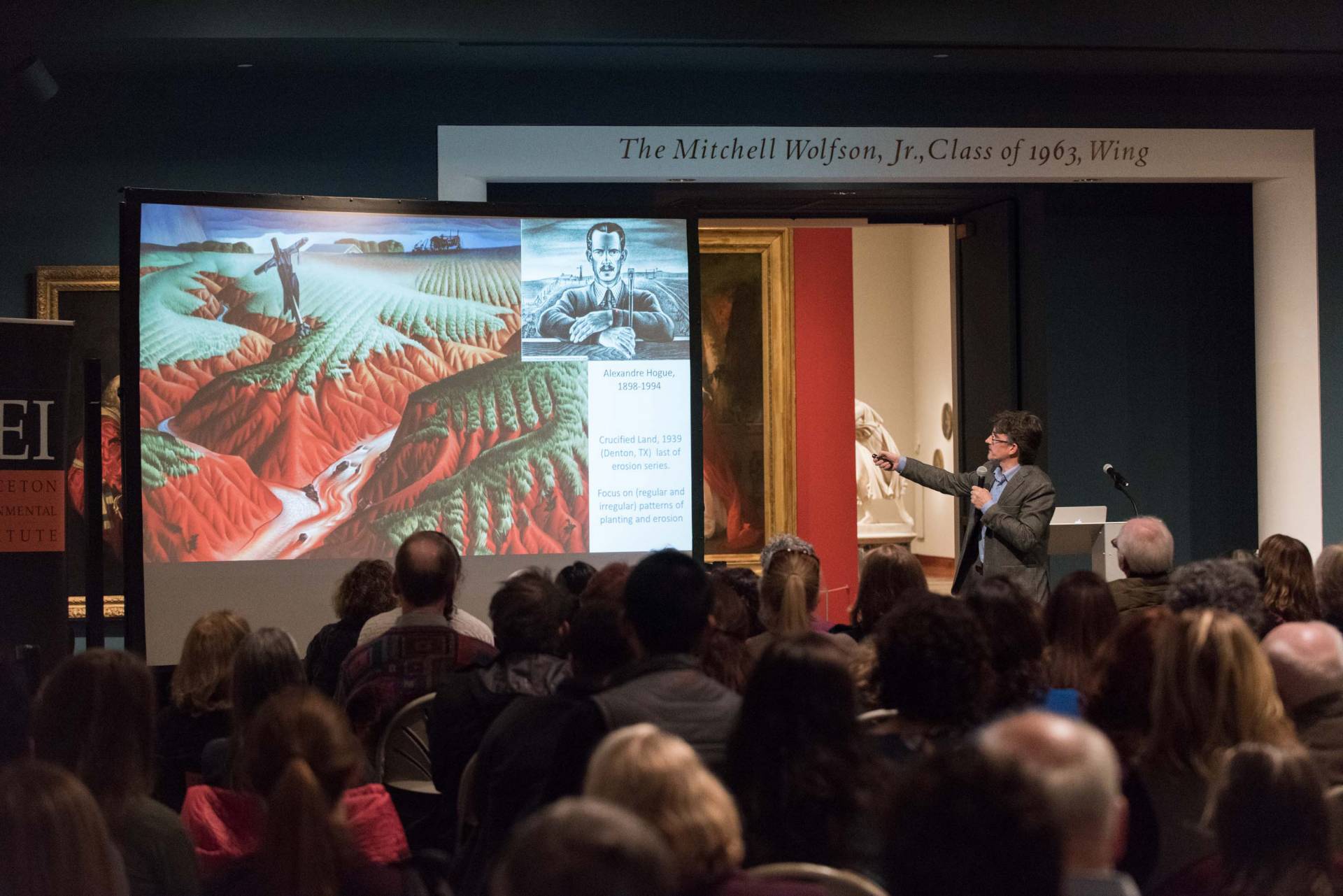Man pointing to a projection of a painting in front of a crowd