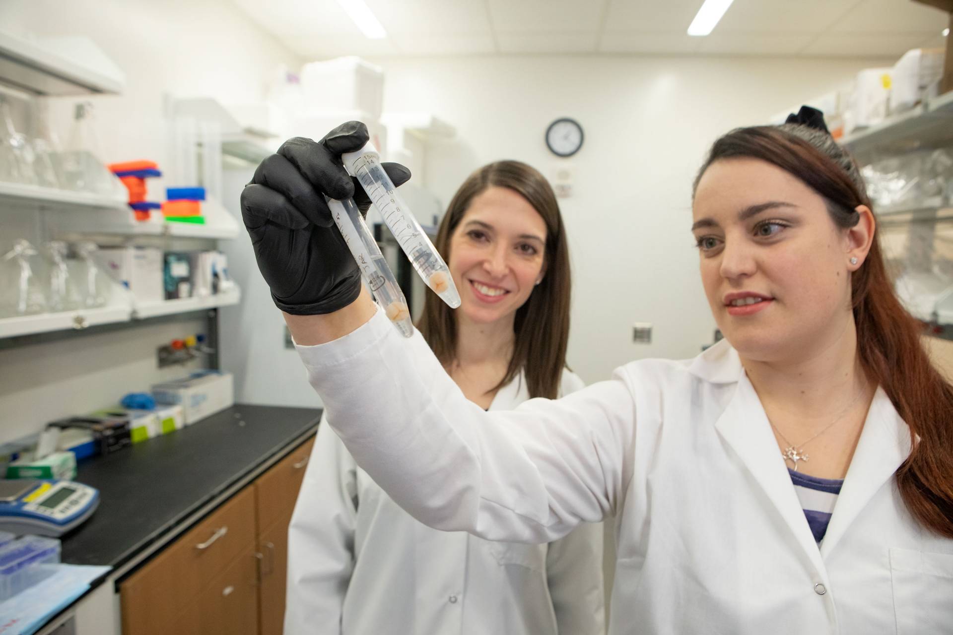 Two women in lab coats look at a test tube