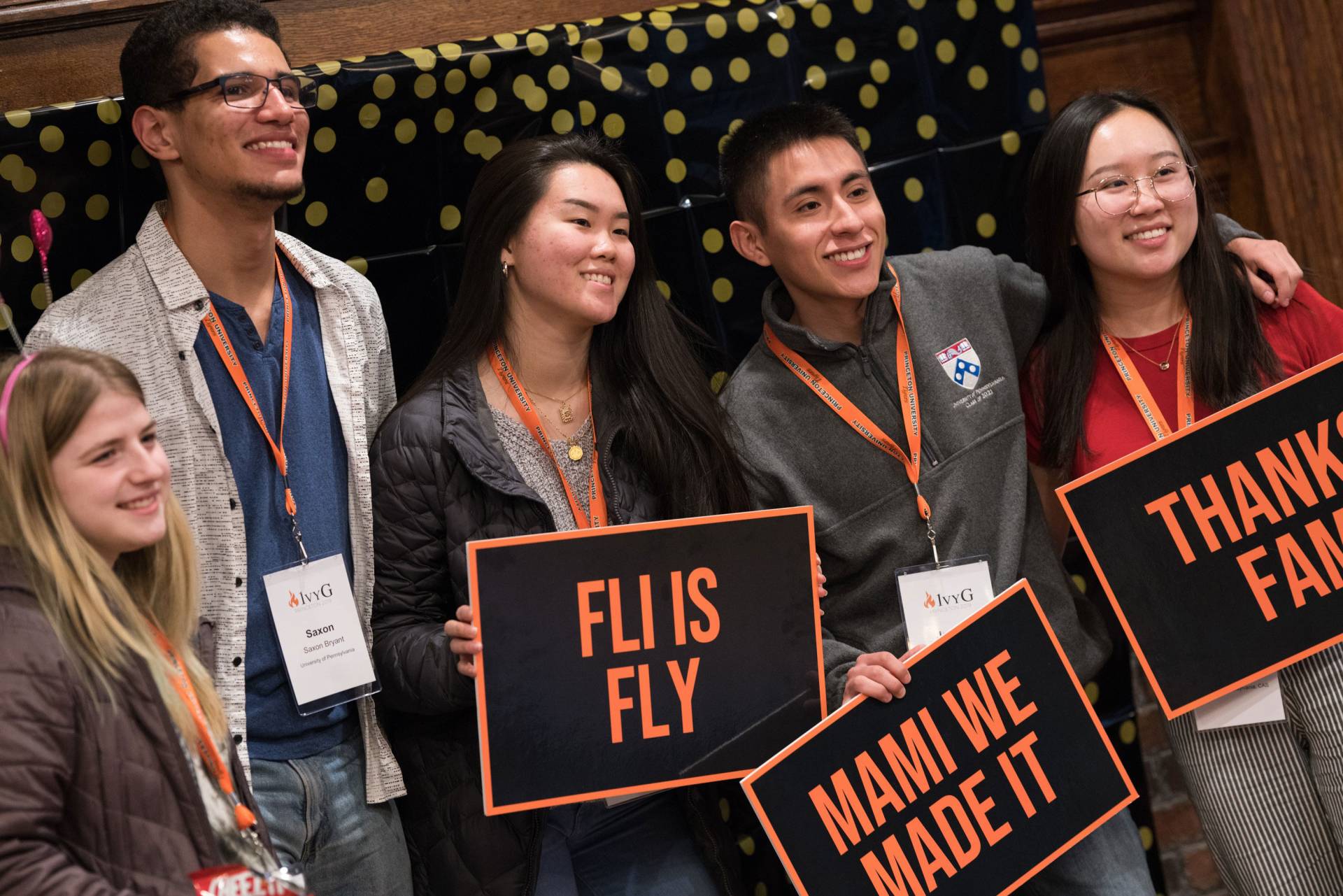 Students pose with signs that say, "FLI is fly," "Mami We Made It," and "Thanks Family"