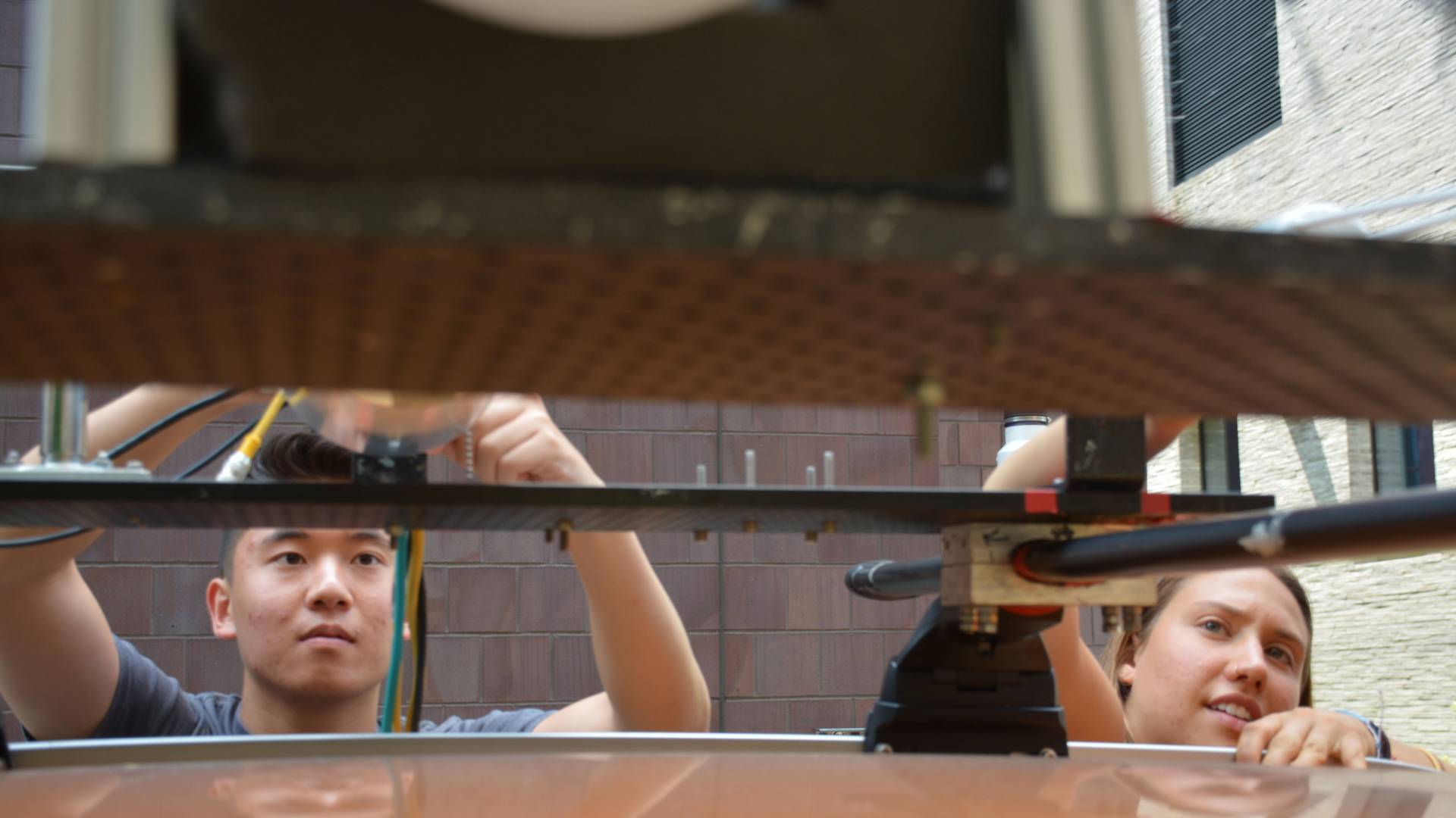 two students ajust the machinery on the roof of a car