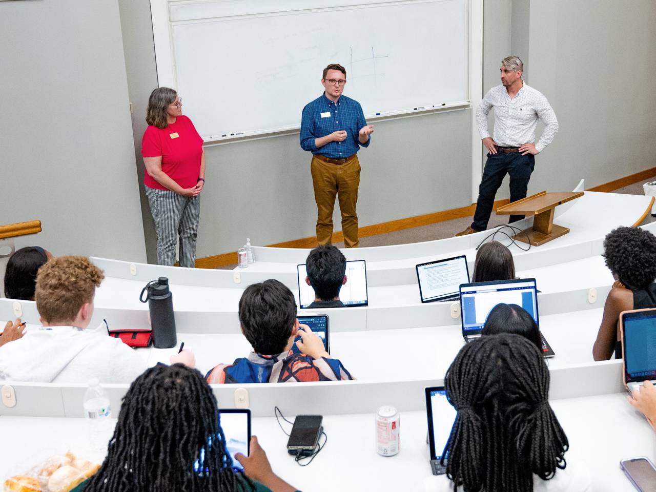 Students in an auditorium with three people in front speaking.