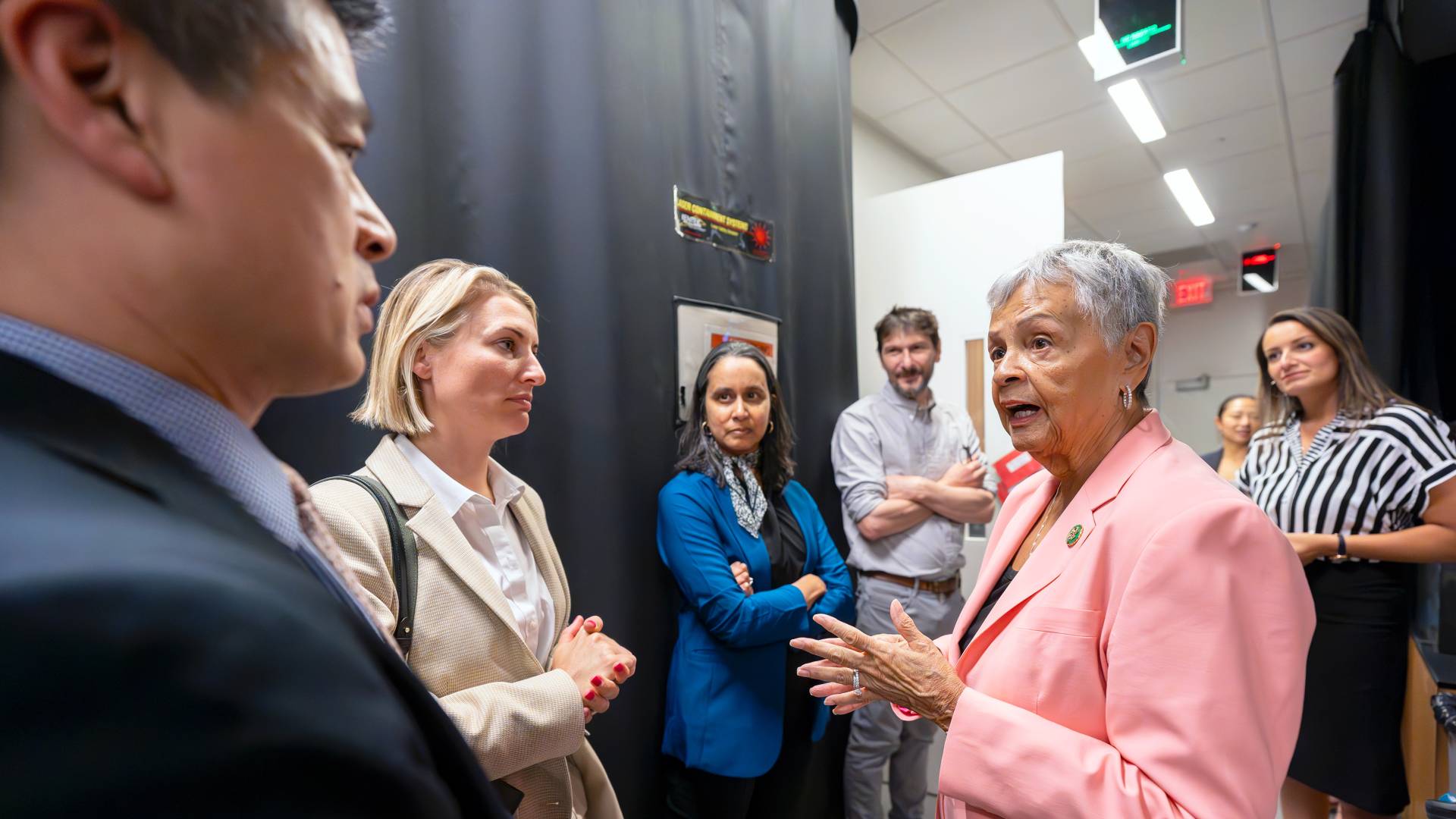 Bonnie Watson Coleman standing in the NIH lab in front of Mala Murthy and others while speaking with Dr. John Ngai
