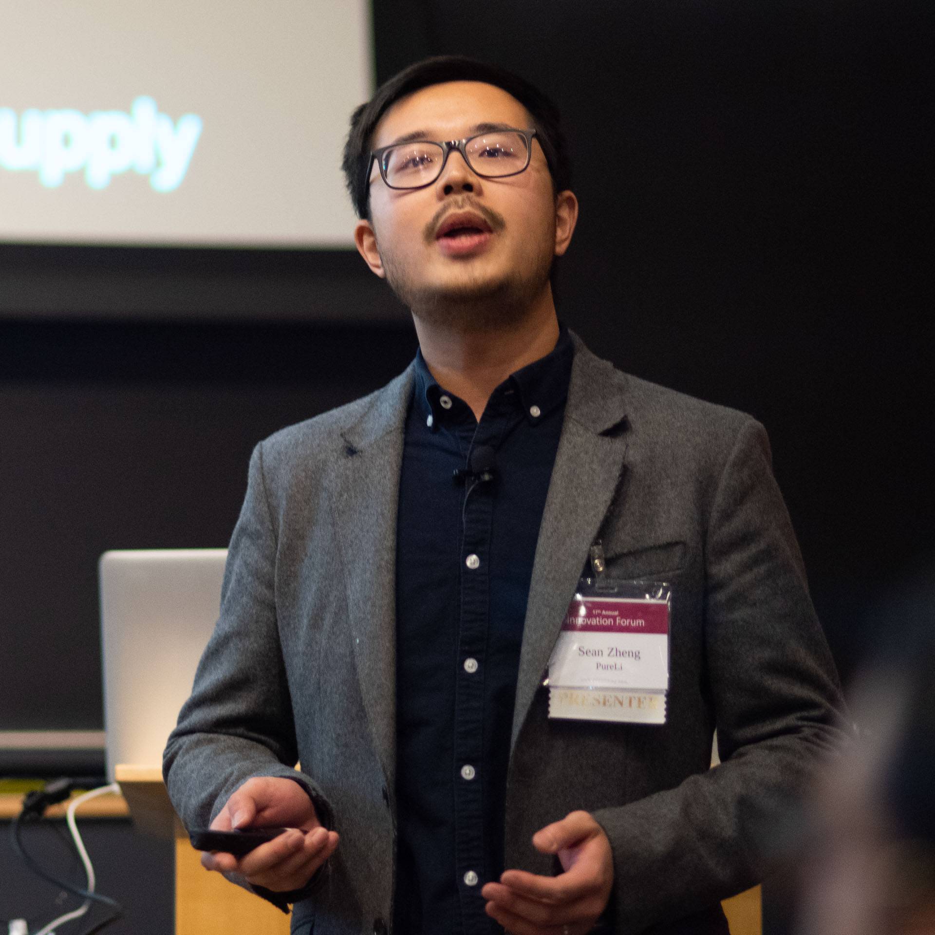 A man in glasses and a blazer speaks at a conference.