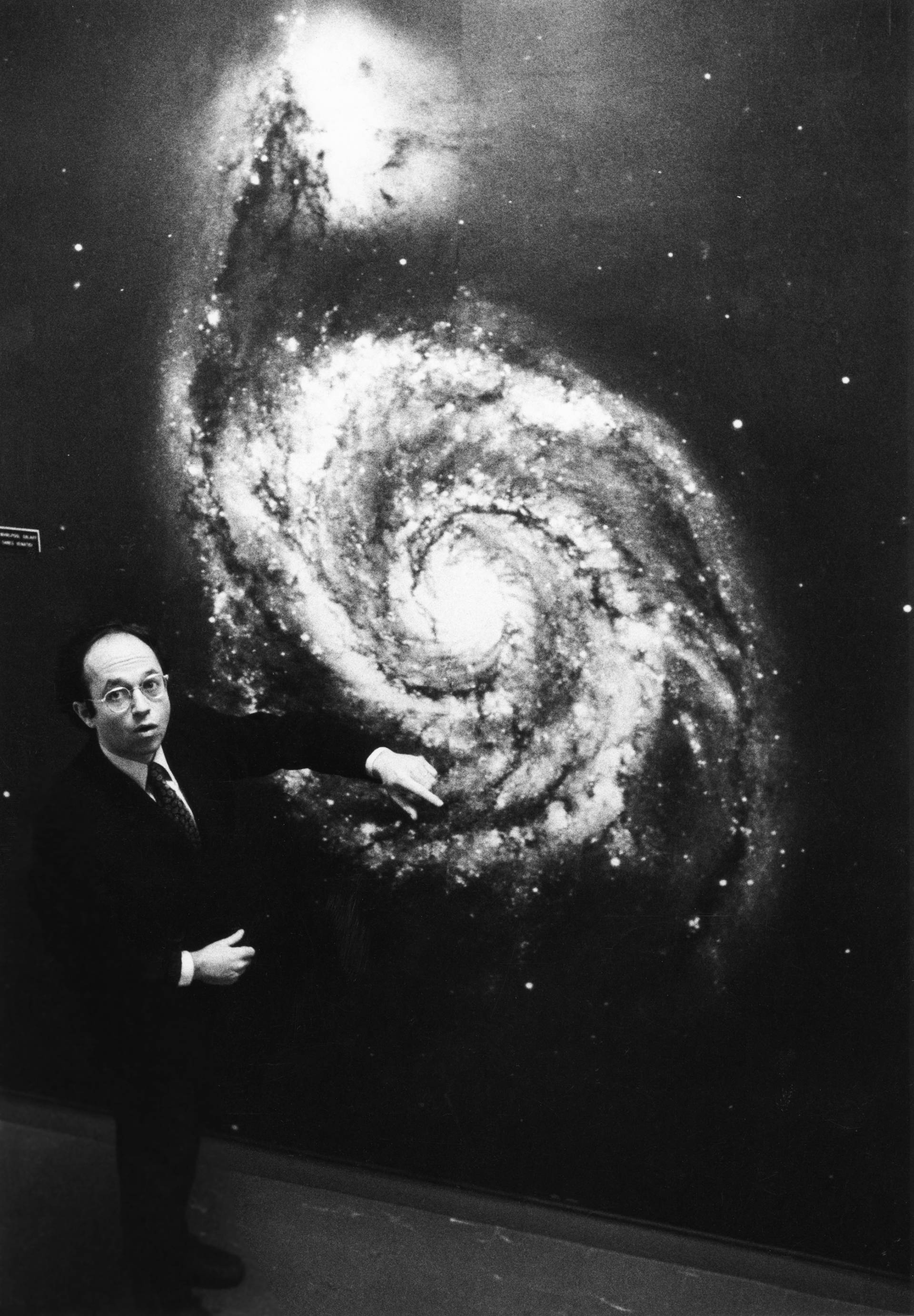 Jeremiah Ostriker stands before a backdrop that depicts a spiraling galaxy. 
