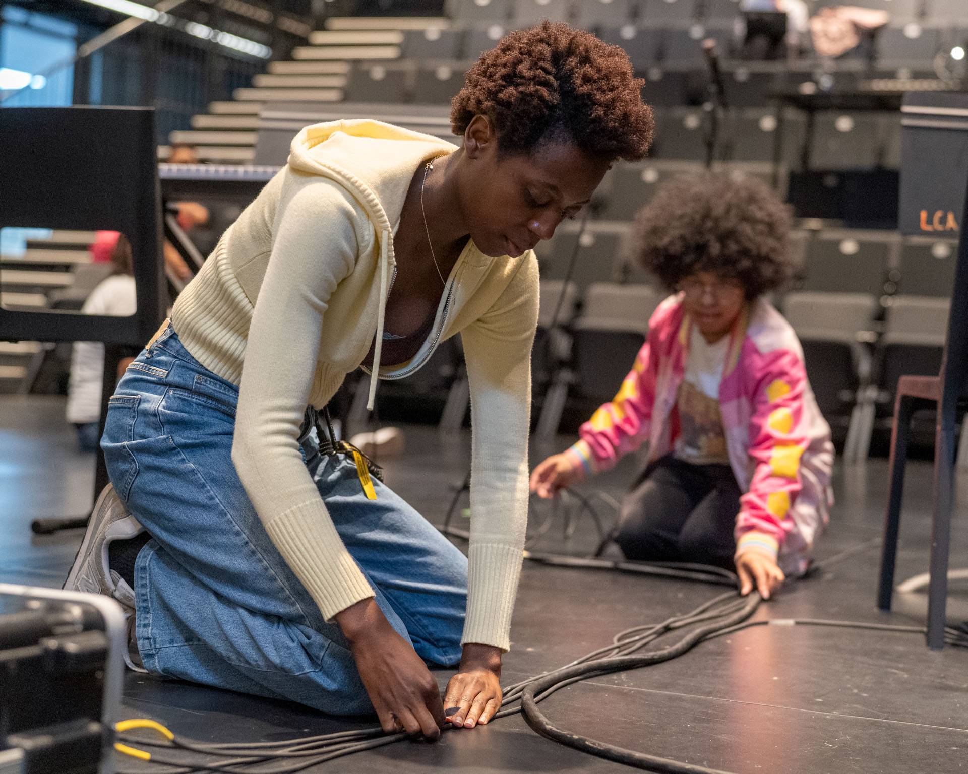 Students tape down sound cables for a live band setup.