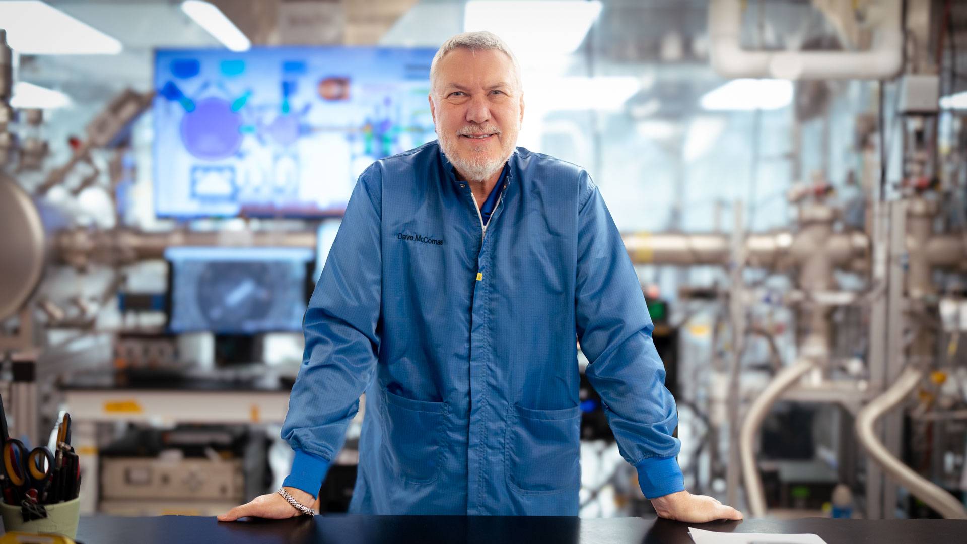 A bearded man in a blue jacket stands in a shiny industrial space.