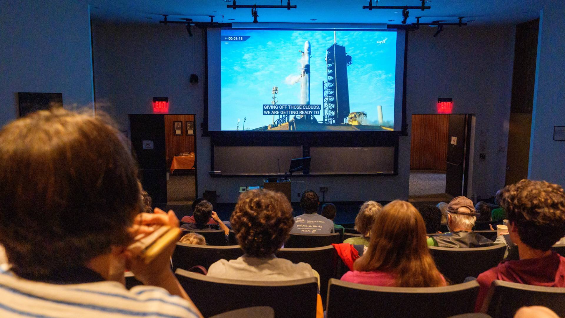 A crowd watches the launch broadcast from an auditorium on campus