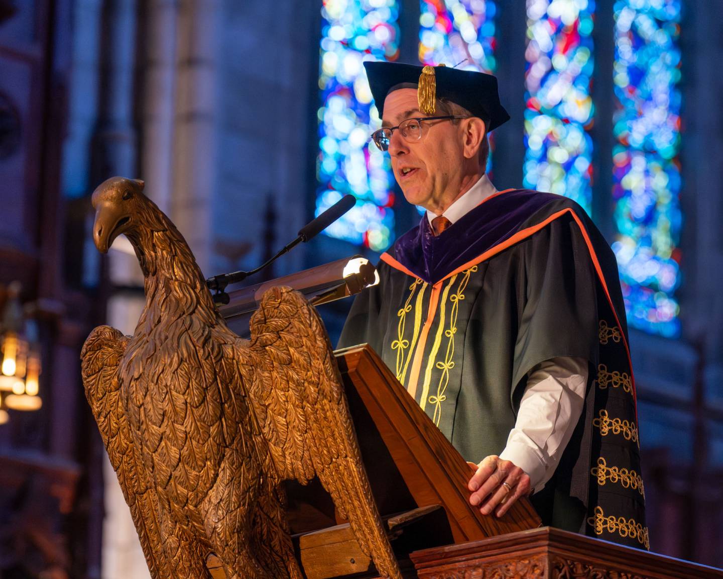The University president speaks at a podium in front of stained glass.