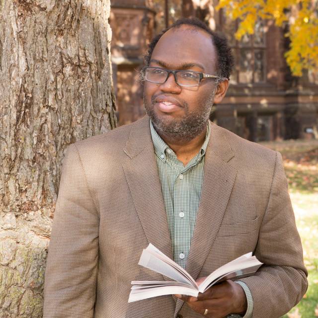 Dan-el Padilla Peralta with book in hand standing by tree